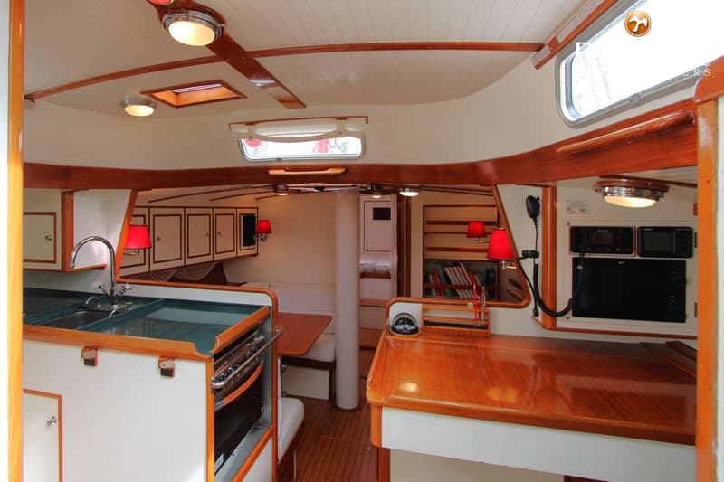 De foto toont het interieur van een boot met een kombuis, navigatiehoek, zithoek en slaapcabine, alles afgewerkt met hout…