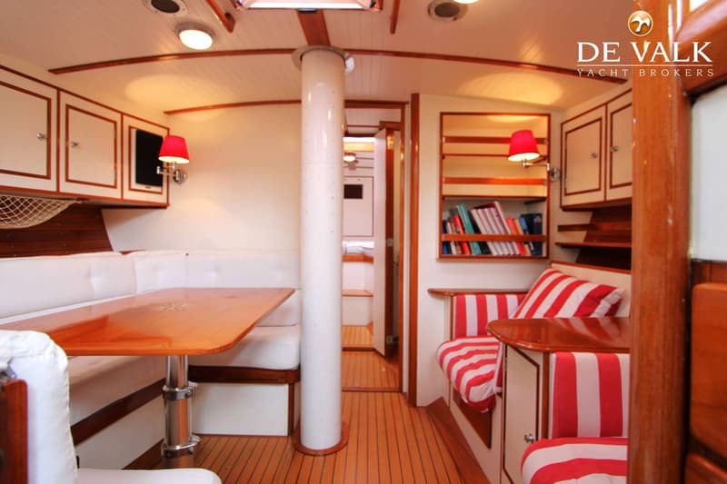 De foto toont het interieur van een boot met een houten tafel, witte banken en rood-wit gestreepte kussens. — Huisman 45