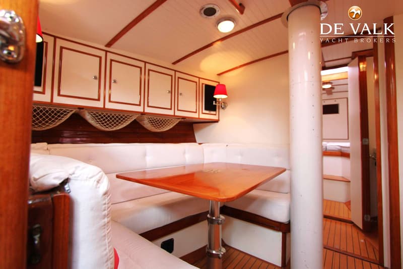 Een interieur van een boot met een houten tafel, witte banken, kasten en een rode lamp. — Huisman 45