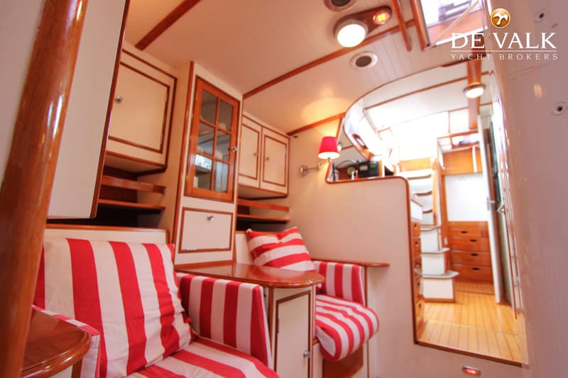 Een interieur van een boot met houten lambrisering, witte wanden, rood-wit gestreepte kussens en een houten vloer.