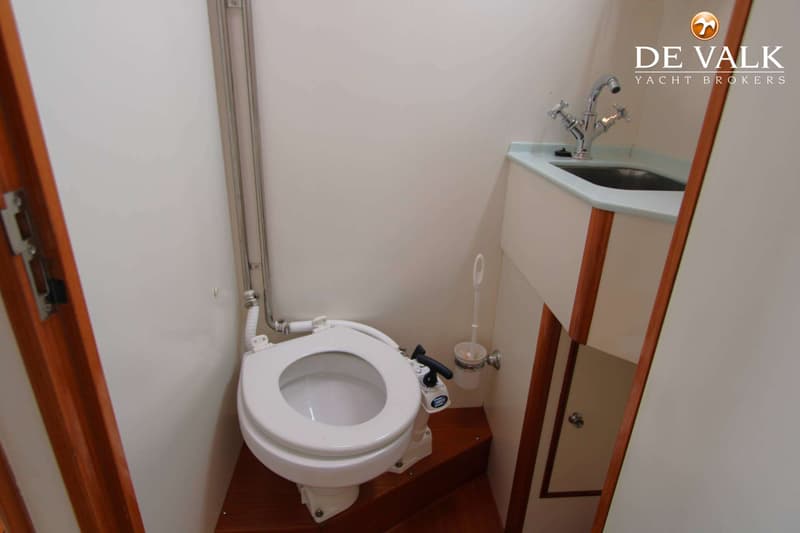Een toiletruimte met een wit scheepstoilet, een wastafel met kraan en een toiletborstel.
