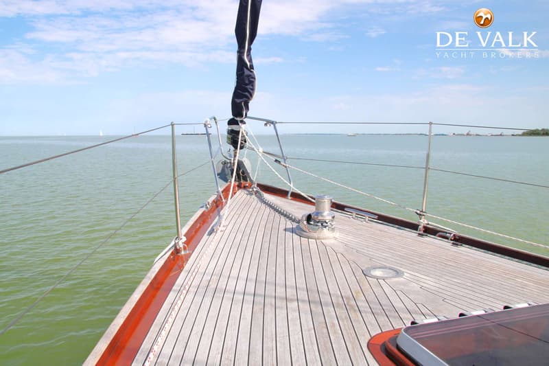 De foto toont de boeg van een zeilboot met een houten dek, een ankerlier en een opgerold zeil. — Huisman 45