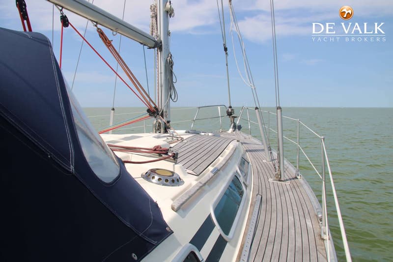 Een zeilboot met een blauwe buiskap en een houten dek vaart op open water met windmolens aan de horizon. — Moody 336