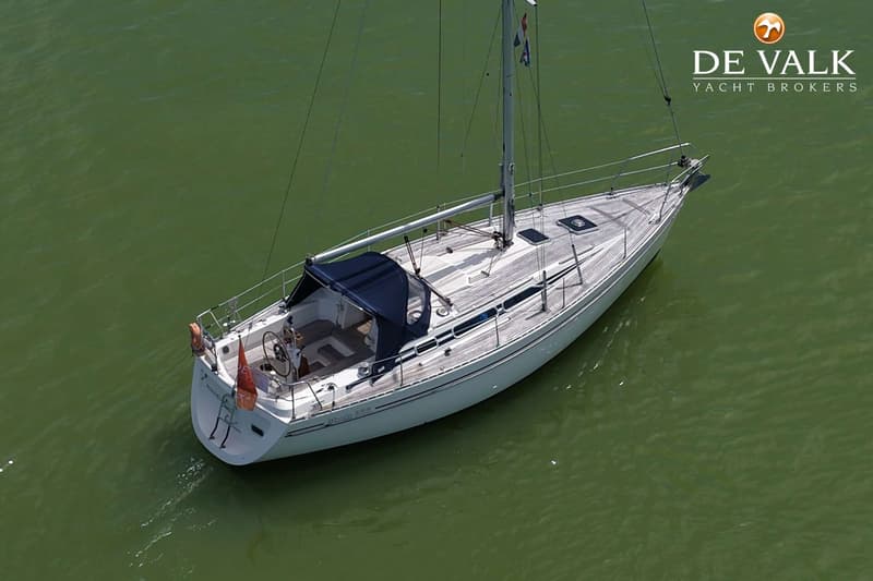 Een witte zeilboot met een donkerblauwe buiskap en een houten dek, drijvend op groen water. — Moody 336