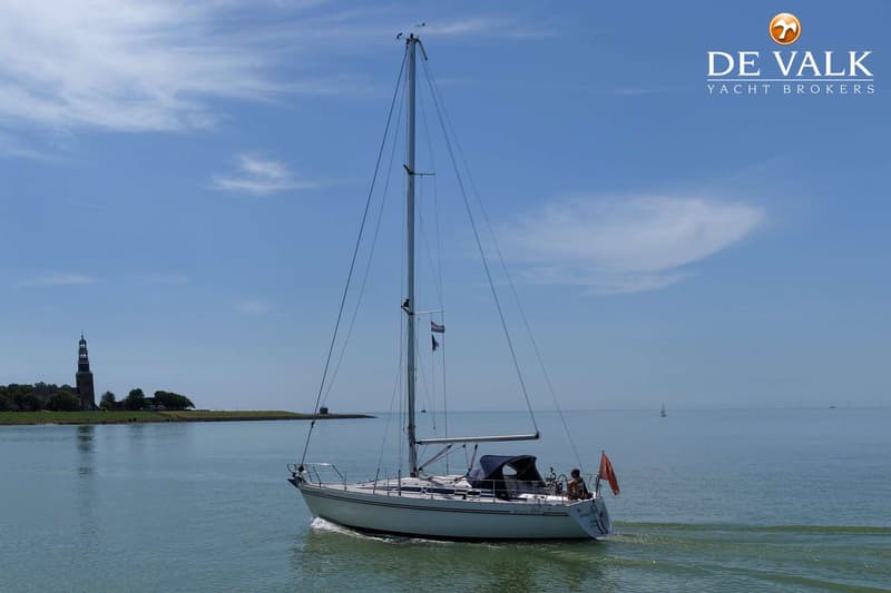 Een witte zeilboot vaart op rustig water onder een blauwe hemel, met een toren op de achtergrond. — Moody 336