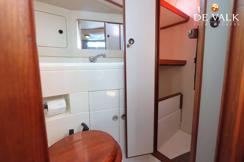 Een badkamer met een wastafel, spiegel, toilet met houten zitting, toiletrolhouder en een aparte doucheruimte.