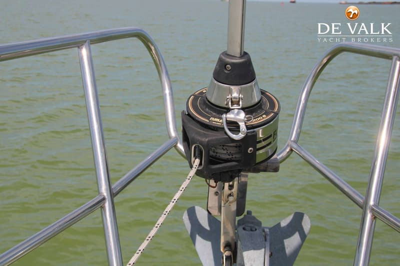 Een voorstagrolfokinstallatie met een opgerold zeil en een anker op de boeg van een boot, met water op de achtergrond.