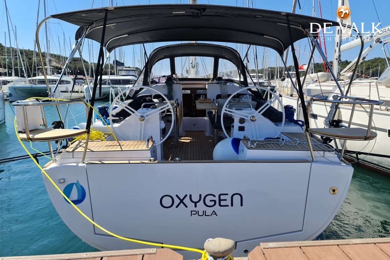 Een witte zeilboot met de naam "OXYGEN PULA" op de spiegel, afgemeerd aan een houten steiger. — Elan Impression 45.1