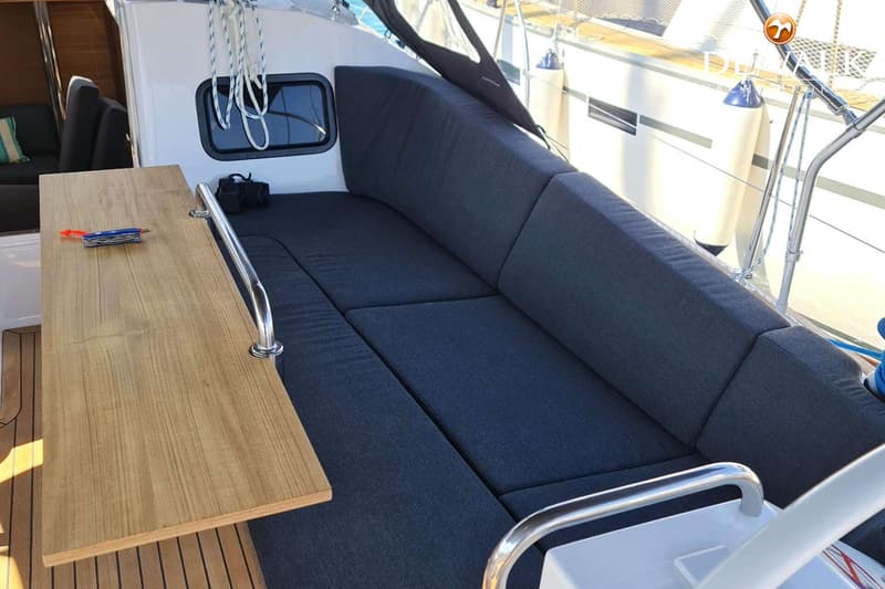 Een houten tafel en een donkerblauwe bank met kussens zijn zichtbaar in de kuip van een boot. — Elan Impression 45.1