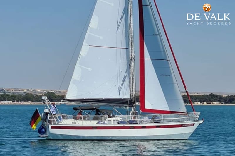 Een witte zeilboot met rode strepen op de romp en rode accenten op de zeilen vaart op blauw water. — Custom Built Sloop