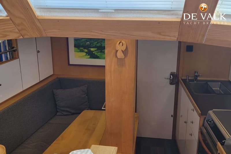 De foto toont een interieur van een boot met een zithoek, een tafel, een kombuis en houten balken. — Custom Built Sloop