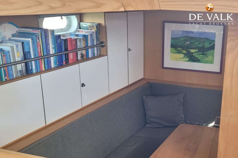 Een interieur met een bank, een tafel, een boekenplank met boeken, kasten en een schilderij aan de muur.