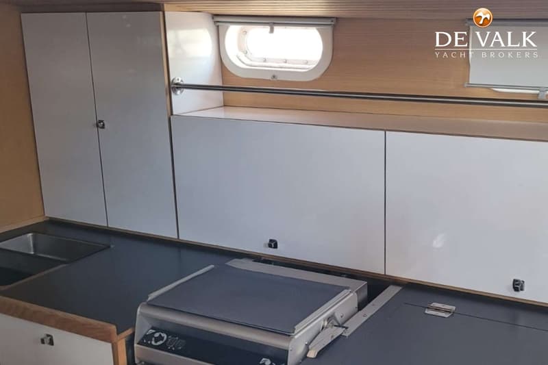 Een interieur van een boot met een aanrecht, twee wasbakken, een kookplaat en witte kasten. — Custom Built Sloop