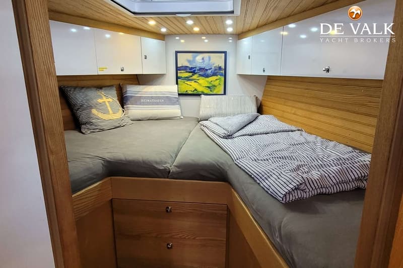 De foto toont een kajuit met twee bedden, houten panelen, witte kasten en een schilderij aan de muur. — Custom Built Sloop