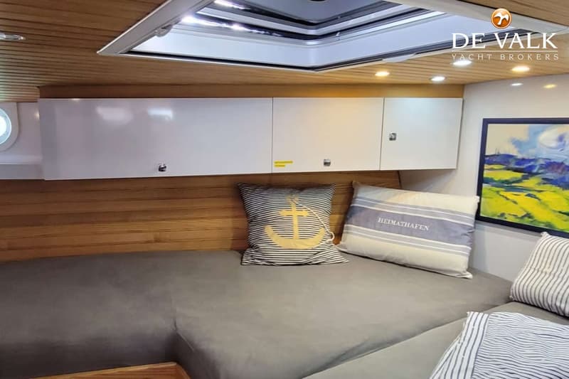 Een kajuit met een bed, kussens, houten lambrisering, witte kasten en een dakraam. — Custom Built Sloop