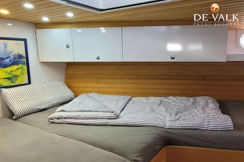 Een kajuit met een bed, gestreepte kussens en dekens, witte kasten en een schilderij aan de muur. — Custom Built Sloop