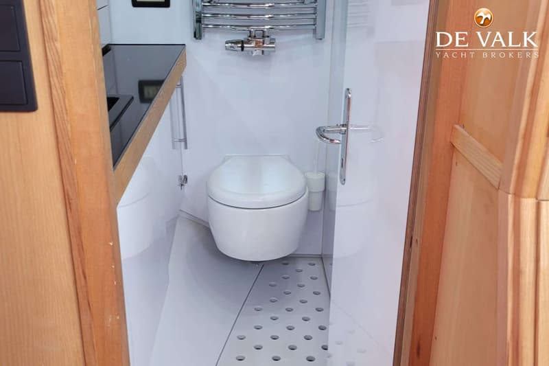 Een witte toiletruimte met een toilet, een handdoekrek, een wastafel en een houten deur.