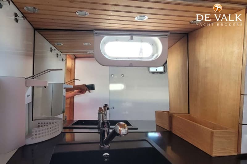Een interieur van een boot met een houten plafond, een gootsteen, een kraan en een patrijspoort. — Custom Built Sloop