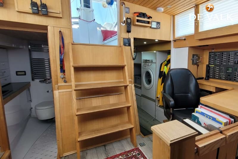 Een interieur van een boot met houten lambrisering, een trap, een toiletruimte, een wasmachine en een stuurstoel.