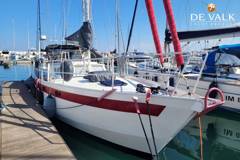 Een witte zeilboot met een rode streep ligt afgemeerd aan een houten steiger in een jachthaven. — Custom Built Sloop