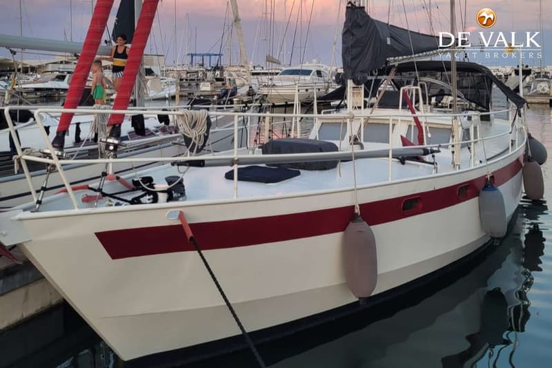 Een witte zeilboot met een rode streep en zwarte romp ligt in een haven met andere boten. — Custom Built Sloop
