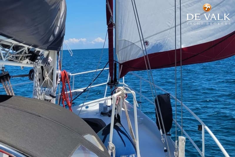 Een zeilboot vaart op open water met een deels opgerold zeil en een wit-rood zeil. — Custom Built Sloop