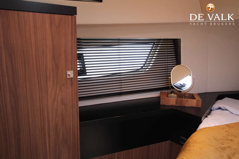 Een slaapkamer in een boot met een houten kast, een raam met jaloezieën, een spiegel op een houten dienblad en een bed.