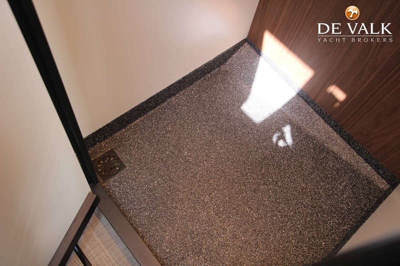 Een detailfoto van een douchebak met een bruin gespikkeld oppervlak en een metalen afvoerputje.