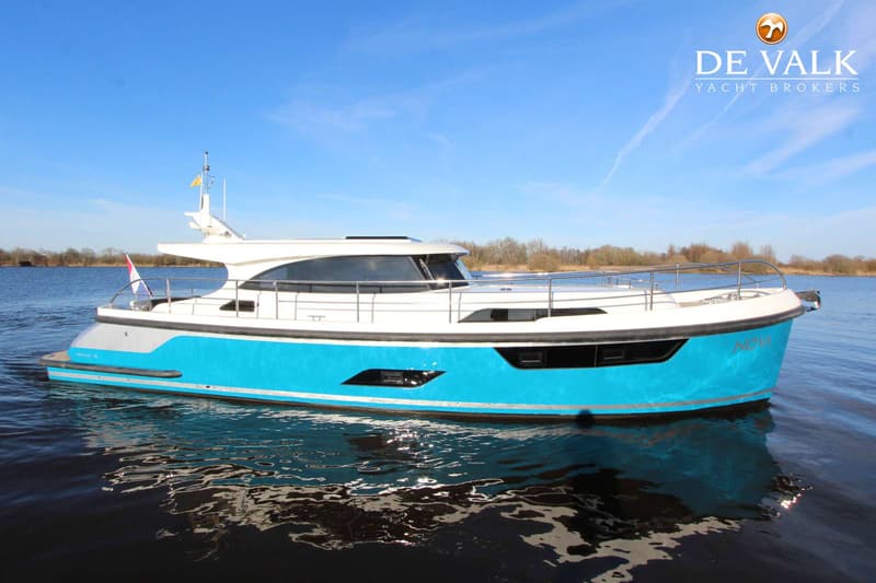 Een witte en turquoise boot met de naam "NOVA" op de boeg vaart op rustig water onder een helderblauwe lucht. — Vripack 45 OK