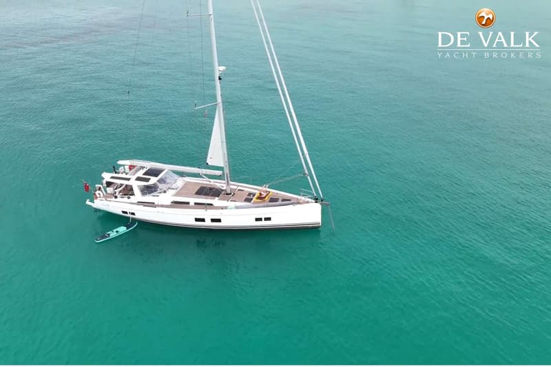 Een witte zeilboot met een opblaasbaar paddleboard ernaast ligt in helder turquoise water. — Hanse 588