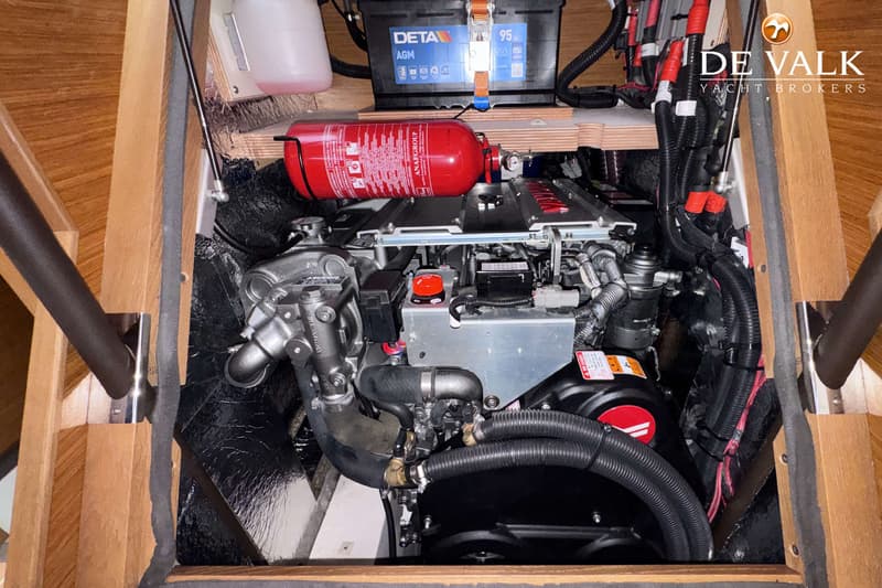 Een detailfoto van een scheepsmotor met een brandblusser en een accu erboven, omringd door houten panelen.