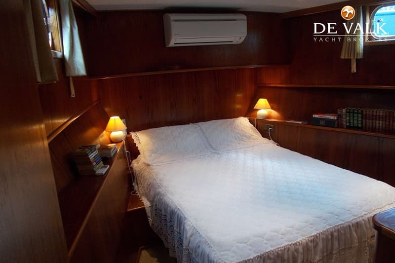 Een slaapkamer met een tweepersoonsbed, twee nachtlampjes, een airconditioningunit en houten wandpanelen.