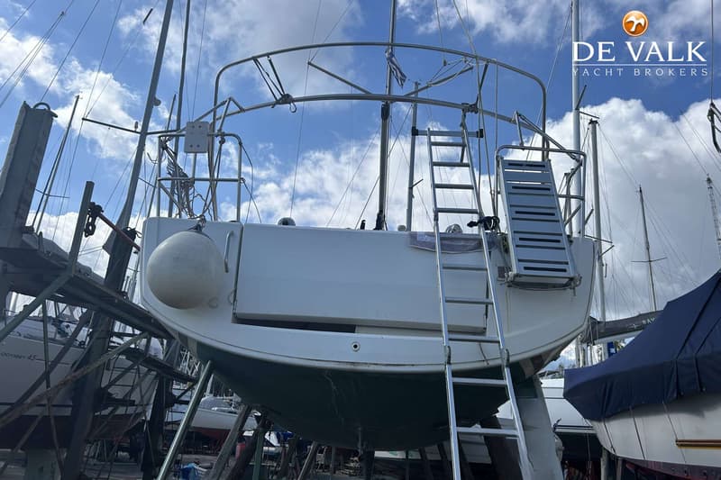 Een witte zeilboot staat op de wal, ondersteund door stutten, met een ladder en een gangway aan de achterzijde.