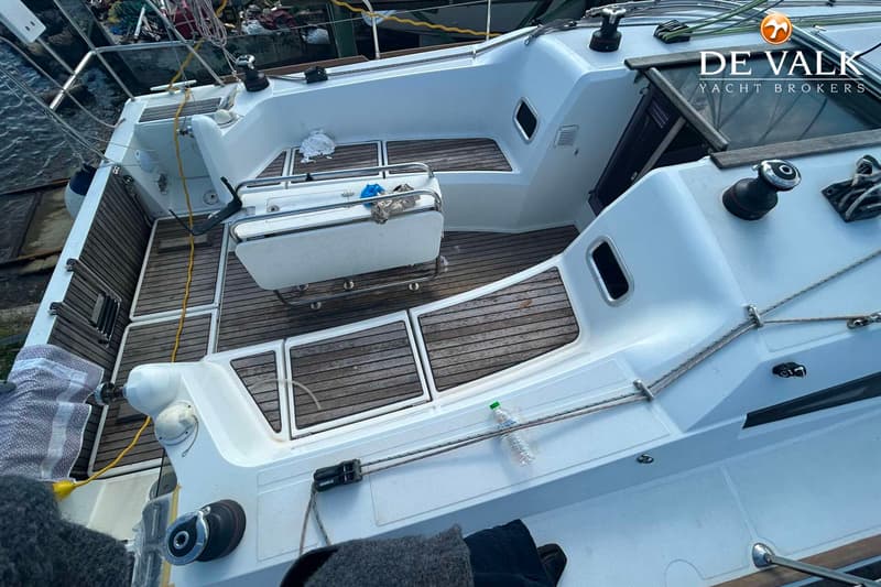 Een bovenaanzicht van de kuip van een witte zeilboot met teakhouten dekdelen, een opklapbare tafel en diverse lijnen en…
