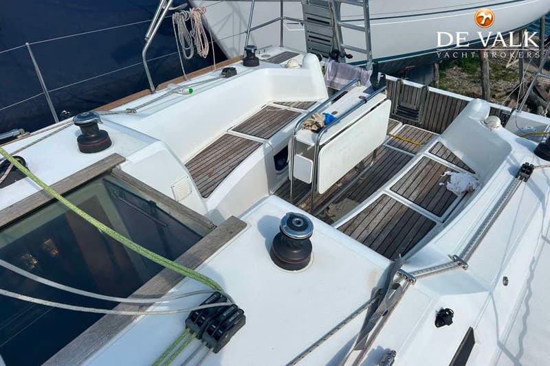 Een bovenaanzicht van de kuip van een witte zeilboot met teakhouten vloer en banken, met een opklapbare tafel.