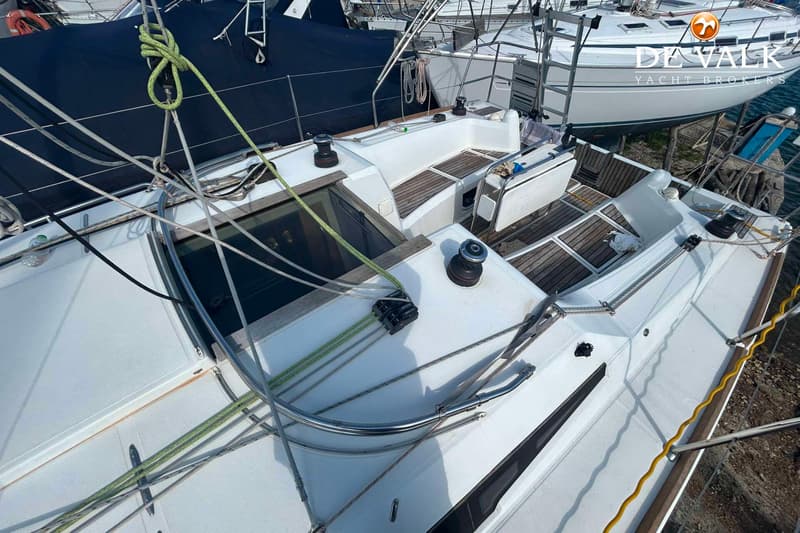 Een bovenaanzicht van het dek en de kuip van een witte zeilboot met houten details en diverse lijnen.