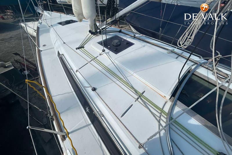 Een bovenaanzicht van het dek van een witte zeilboot met touwen, een luik en een logo van De Valk Yacht Brokers.