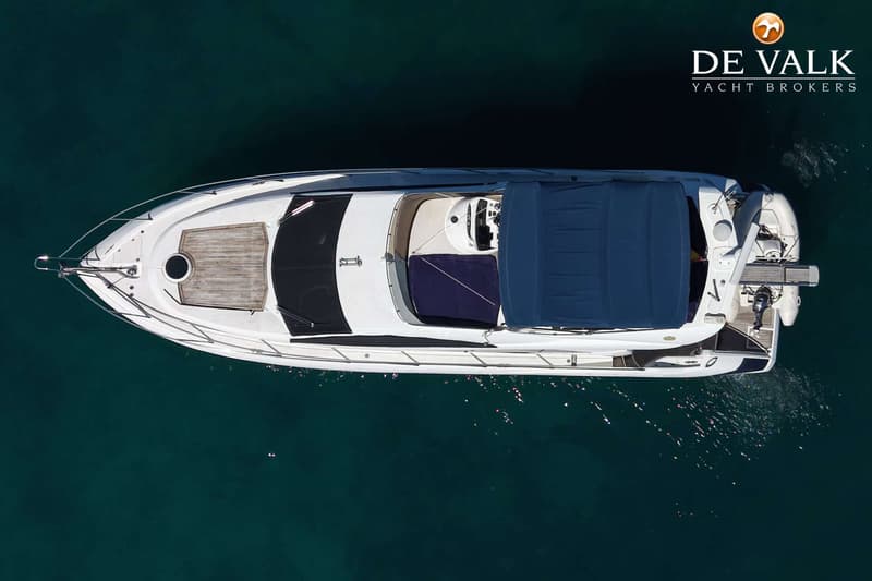 Een witte motorboot met een blauwe bimini en een houten dekdeel, gezien van bovenaf op donkergroen water.