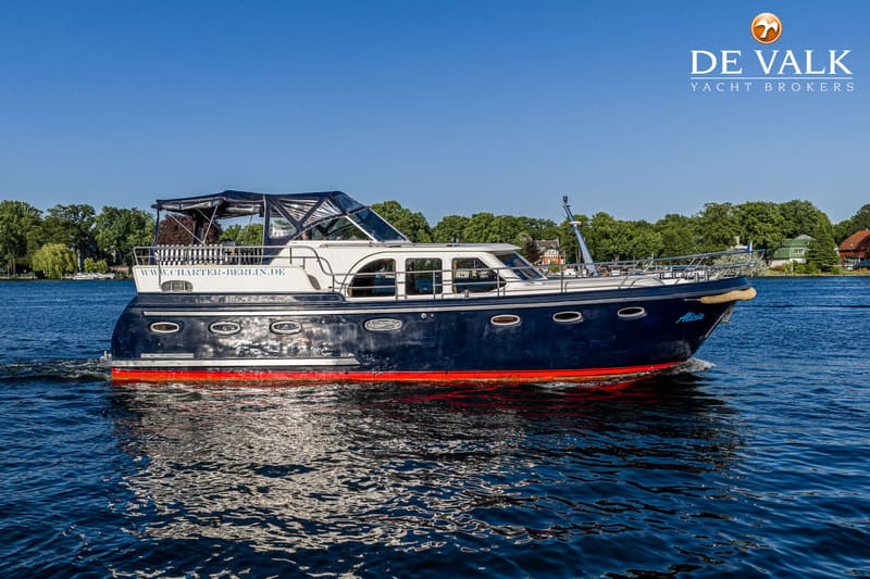 Een blauw-witte motorboot met rode onderkant vaart op een waterweg met bomen en huizen op de achtergrond.