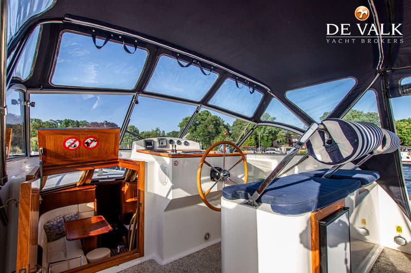 De foto toont het interieur van een boot met een houten stuurwiel, een kajuitingang en een instrumentenpaneel.