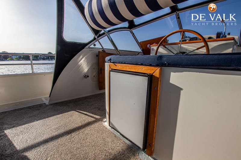 De foto toont een interieur van een boot met een stuurwiel, een gestreepte luifel en een koelkast. — De Drait Deluxe 42