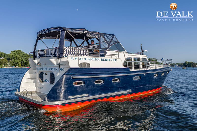 Een blauw-witte motorboot met een rode onderkant vaart op een zonnige dag over het water. — De Drait Deluxe 42