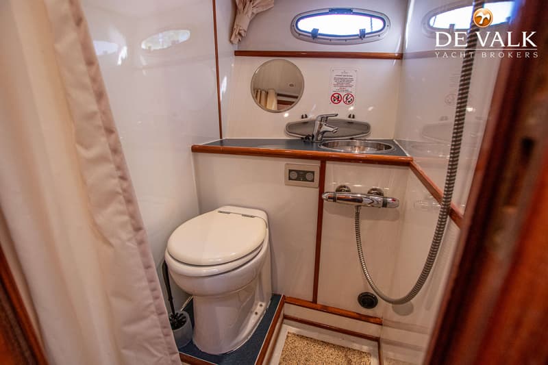 De foto toont een badkamer in een boot met een toilet, wastafel, spiegel, douche en een patrijspoort. — De Drait Deluxe 42