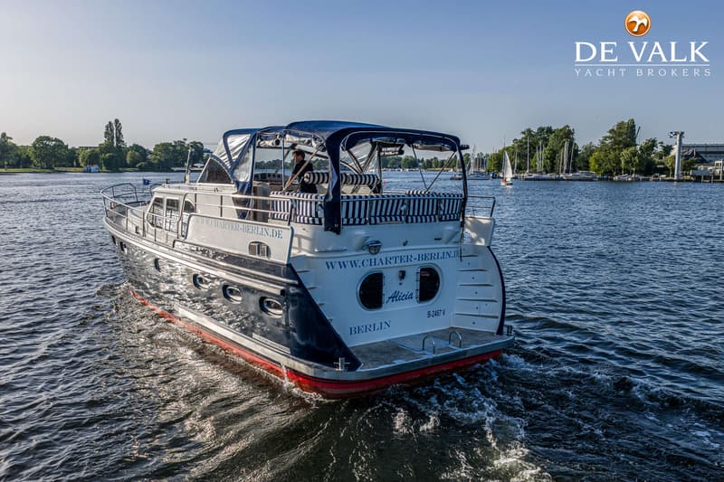 Een motorjacht met de naam "Alicia" en "BERLIN" erop, vaart op open water met een persoon aan het roer.