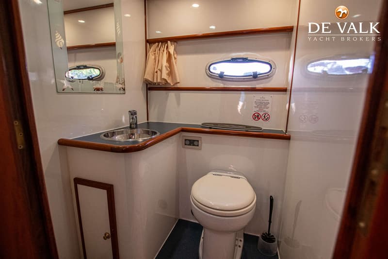 Een badkamer met een wastafel, spiegel, toilet, patrijspoort en een bordje met instructies.