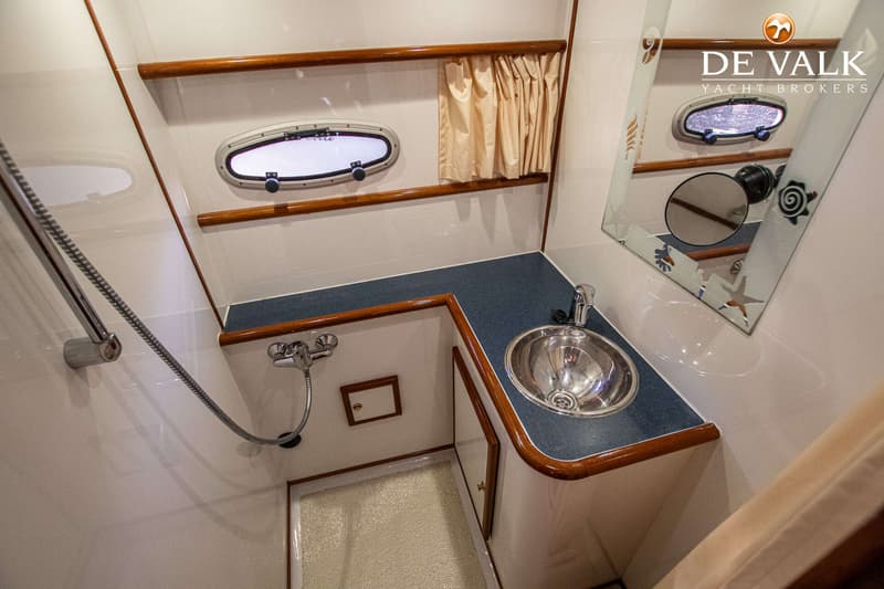 Een badkamer aan boord met een wastafel, spiegel, douche en patrijspoorten.