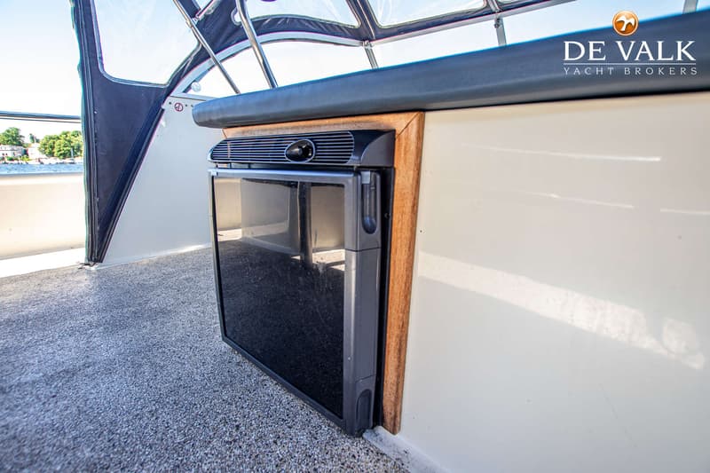 Een ingebouwde koelkast met een zwart glazen deur en een houten omlijsting is zichtbaar op een boot. — Babro Newline 1290