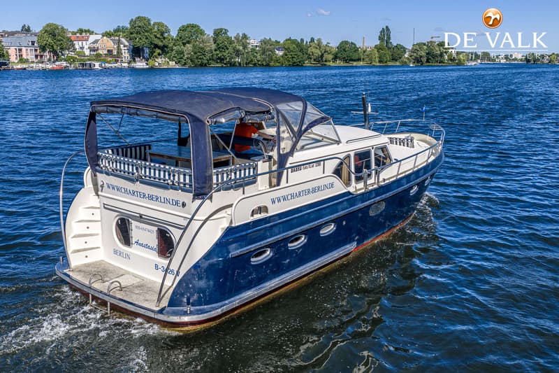 Een blauw-witte motorboot met de naam "Anastasia" en "WWW.CHARTER-BERLIN.DE" vaart op een waterweg. — Babro Newline 1290
