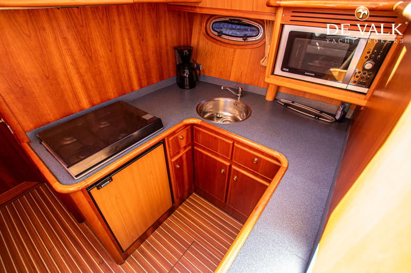 De foto toont een scheepskeuken met een kookplaat, spoelbak, koelkast, magnetron en koffiezetapparaat.