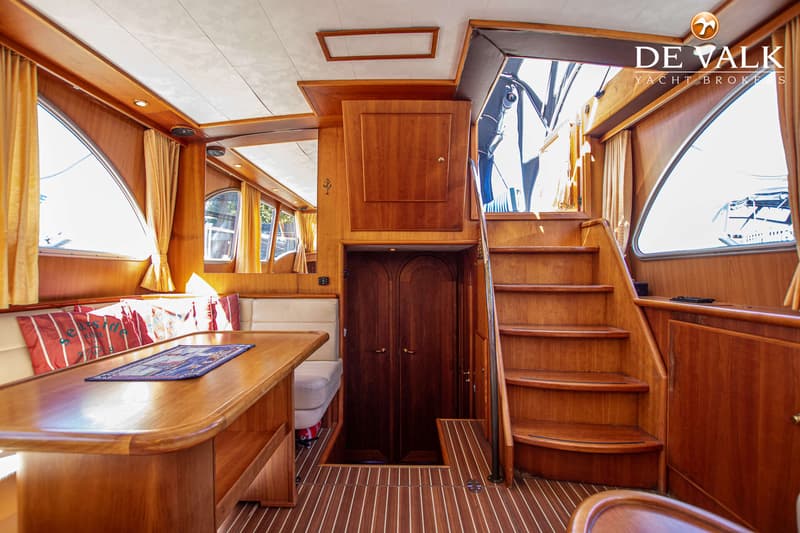 Een houten interieur van een boot met een trap, een tafel met banken en een deur. — Babro Newline 1290